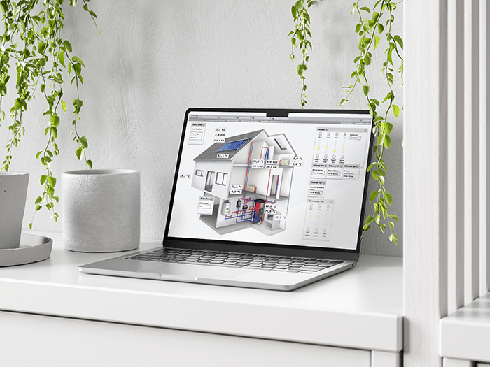 Ein Laptop auf einem weißen Schreibtisch zeigt eine digitale Gebäudediagramm-Anwendung zur Heizungs- und Energiesteuerung. Das dargestellte Haus enthält Beschriftungen und Temperaturangaben für verschiedene Bereiche und Systeme. Im Hintergrund hängen grüne Pflanzen herab, was eine moderne, nachhaltige Atmosphäre vermittelt